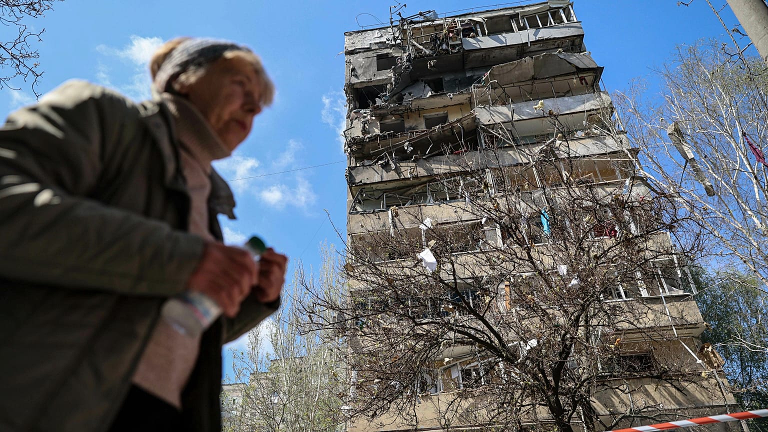 Una donna cammina davanti a un edificio a più piani danneggiato da un attacco russo su un quartiere residenziale di Zaporizhzhia, 22 aprile 2025