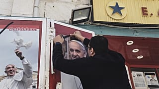 A shop owner in Bethlehem places a black ribbon over a photo of the late Pope Francis after the news of his death, 21 April, 2025