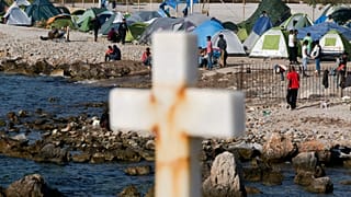 Migrants and refugees walk behind a cross in a camp set up by volunteers near the port of Mytilini, 15 April, 2016