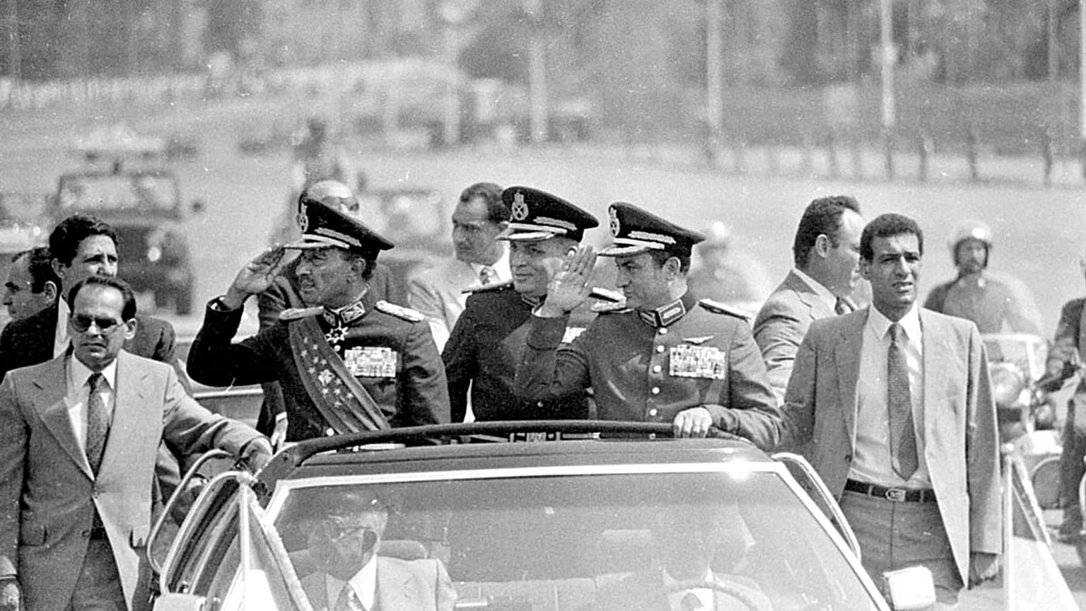 الرئيس المصري أنور السادات, اليسار, يحيي وهو يركب في موكبه إلى موقع العرض العسكري, أكتوبر. 6، 1981 ، في القاهرة