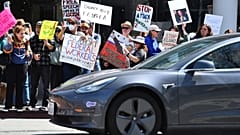 Ένας οδηγός Tesla σταματά σε ένα φανάρι καθώς διαδηλωτές κρατούν πινακίδες στο Walnut Creek της Καλιφόρνια, το Σάββατο 29 Μαρτίου 2025