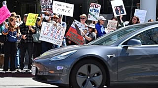 Un autista di Tesla si ferma a un semaforo mentre i manifestanti tengono dei cartelli a Walnut Creek, in California, sabato 29 marzo 2025, durante una manifestazione contro Elon Musk.