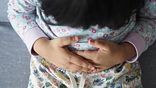 A young child rubs their stomach.