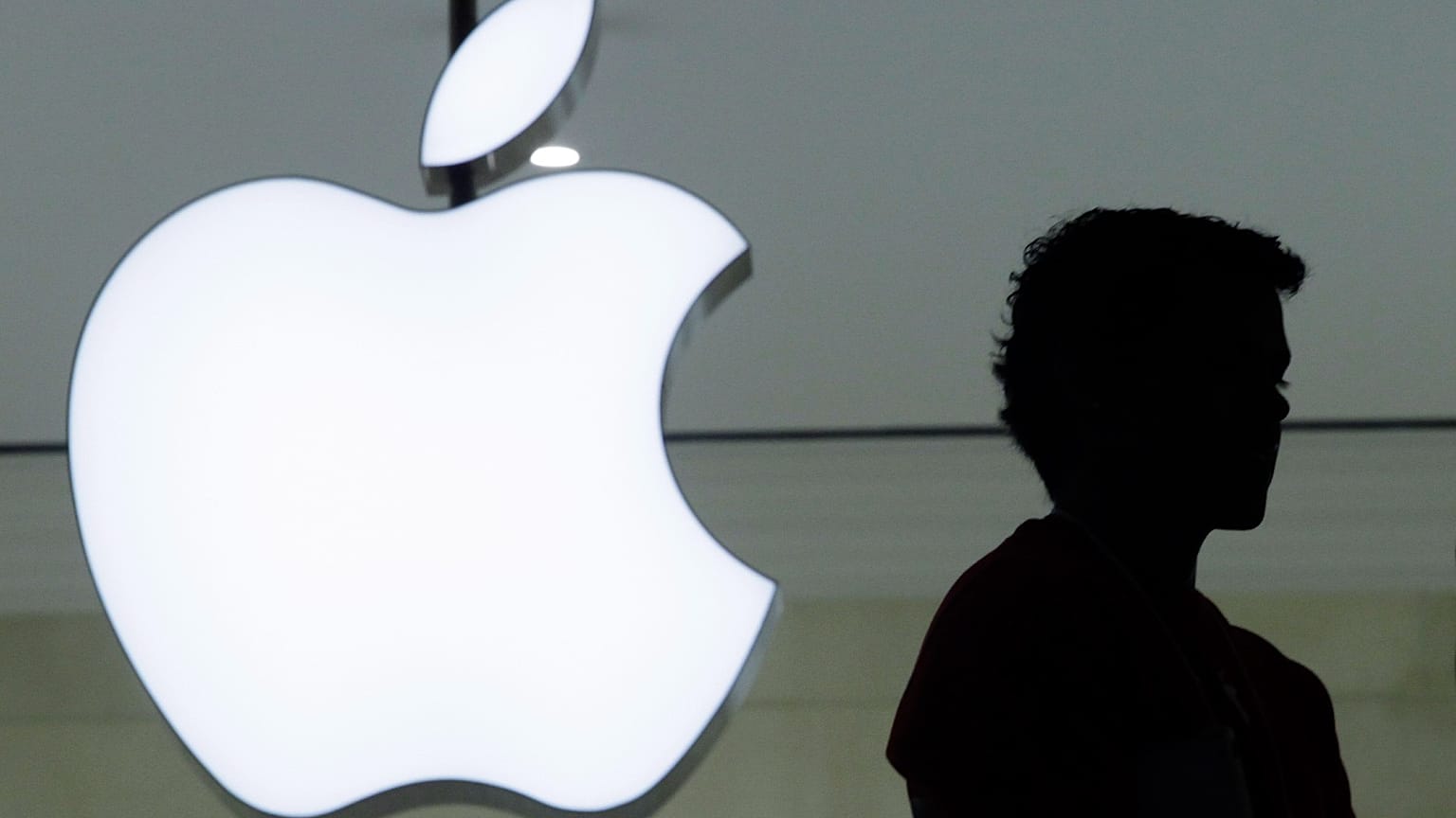 Человек стоит рядом с логотипом Apple в новом магазине компании в Grand Central Terminal в среду, 7 декабря 2011 года, в Нью-Йорке. 