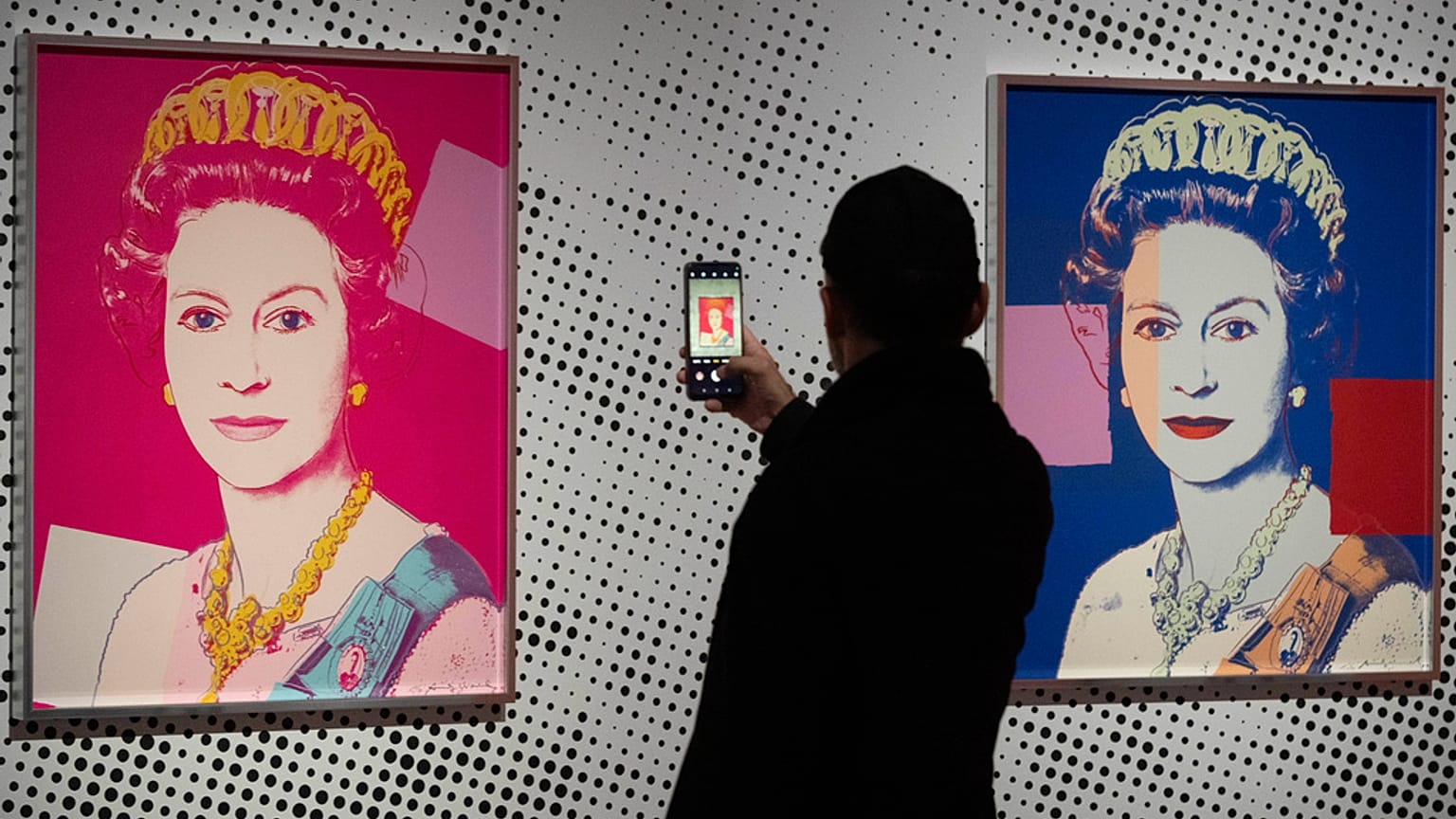 Egy férfi egy képet készít egy II. Erzsébet királynőt ábrázoló szitanyomatról, amely Andy Warhol Reigning Queens (1985) című, négy királynőt ábrázoló tizenhat darabból álló sorozatának egyik darabja.