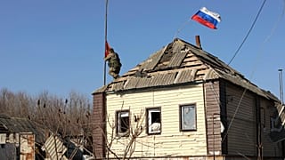 Un soldato russo alza una bandiera sul tetto di una casa vicino alla regione russa di Kursk, dopo che le truppe russe hanno ripreso il territorio