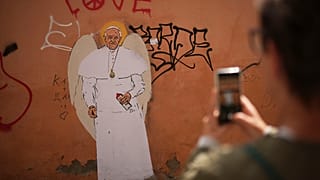 A person takes a picture of a graffiti mural of Pope Francis, near the Vatican, Friday, April 25, 2025. (AP Photo/Francisco Seco)