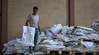 عامل فلسطيني يحمل أحد أكياس الطحين الفارغة في مستودع برنامج الأغذية العالمي في مخيم النصيرات للاجئين ، قطاع غزة ، السبت 26 أبريل / نيسان 2025.