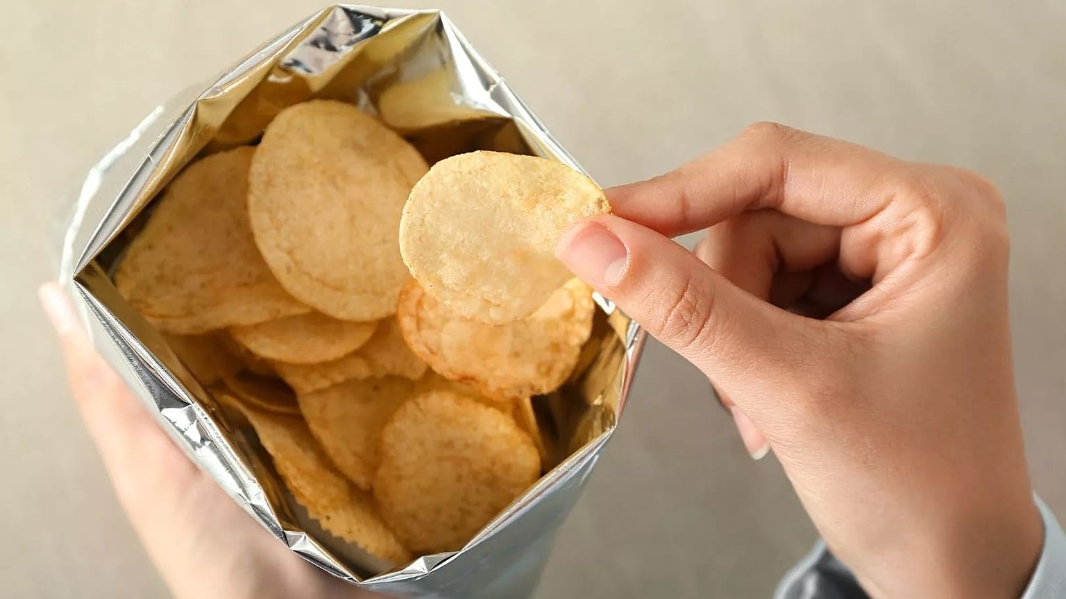 Una persona saca una patata frita de la bolsa.