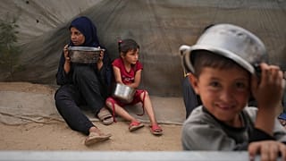 ميرا أبو شعر (5 سنوات) وشقيقتها الكبرى رغد (15 سنة)، تحملان الأواني  بانتظار الحصول على الطعام، في المواصي، على مشارف خان يونس في جنوب قطاع غزة، الخميس 24 أبريل 2025