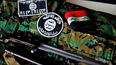 أوسمة لداعش وسوار وسكين من ساحة المعركة بسوريا معروضة فوق زي مموه لميليشيا كردية.