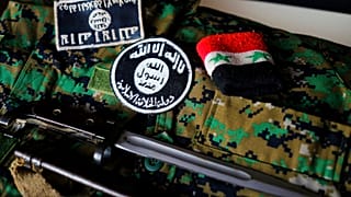 أوسمة لداعش وسوار وسكين من ساحة المعركة بسوريا معروضة فوق زي مموه لميليشيا كردية.