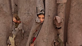 An Afghan refugee girl peers through a torn curtain at the entrance of her home at Kababayan refugee camp in Peshawar, Pakistan, April 8, 2025. 
