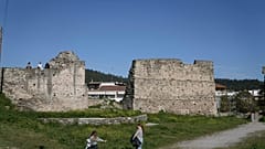 Selanik, Yunanistan'da müzeye dönüştürülen Yedi Kule Hapishanesi'nin dışında bir duvarın üzerinde oturan insanların yanında bir kız çiçek tutuyor.