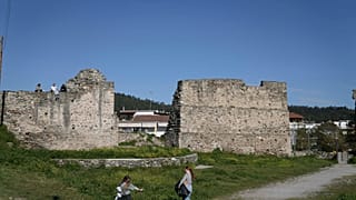 Selanik, Yunanistan'da müzeye dönüştürülen Yedi Kule Hapishanesi'nin dışında bir duvarın üzerinde oturan insanların yanında bir kız çiçek tutuyor.