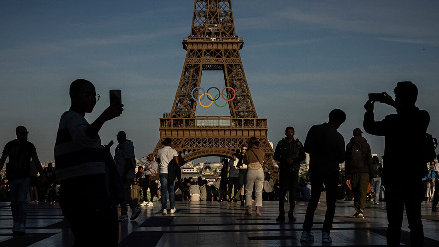 ARQUIVO: ARQUIVO - Pessoas usam os seus smartphones perto dos anéis olímpicos que estão expostos na Torre Eiffel em Paris, a 7 de junho de 2024