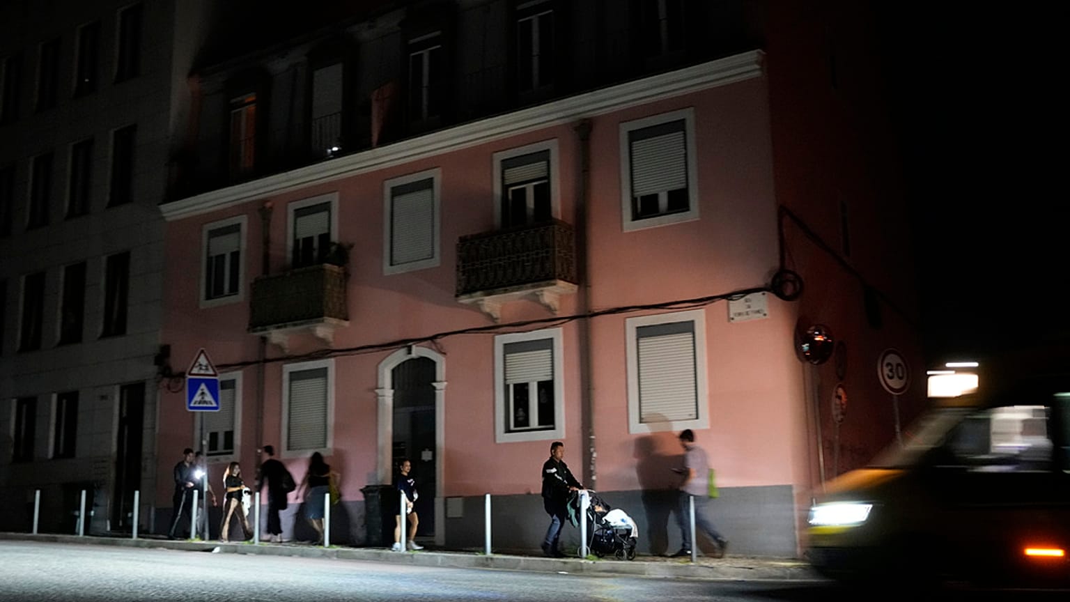 Pessoas caminham ao longo de uma rua sem luz em Lisboa, durante um corte de eletricidade a nível nacional, na noite de segunda-feira, 28 de abril de 2025.