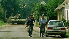 Hırvat polisler Glina'nın dışında devriye gezerken Yugoslav ordusuna ait bir tank arkada görülüyor, 9 Temmuz 1991