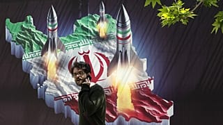 Un passante cammina davanti a uno striscione che mostra il lancio di missili da una mappa iraniana a Teheran, 19 aprile 2024