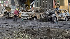 Städtische Arbeiter säubern in der Nähe von verbrannten Autos und einem von einer Drohne verursachten Krater in einem Wohngebiet nach einem russischen Luftangriff in Kiew, Ukraine, Sonntag, 4. Mai 2025.