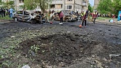Belediye çalışanları, Ukrayna'nın başkenti Kiev'de Rus hava saldırısının ardından yerleşim bölgesinde yanmış araçlar ve bir drone'un açtığı kraterin yanında, 4 Mayıs 2025.