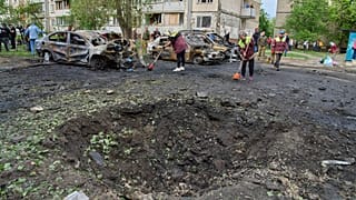 Belediye çalışanları, Ukrayna'nın başkenti Kiev'de Rus hava saldırısının ardından yerleşim bölgesinde yanmış araçlar ve bir drone'un açtığı kraterin yanında, 4 Mayıs 2025.