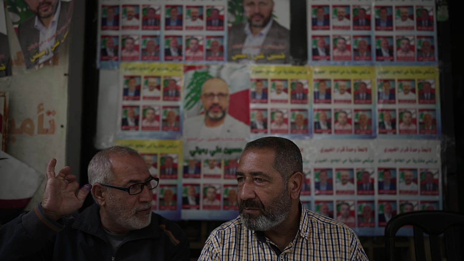Un votante, a la izquierda, muestra su dedo manchado de tinta mientras habla con un amigo frente a carteles de campaña de candidatos a las elecciones municipales 