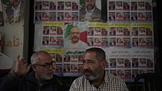 Un votante, a la izquierda, muestra su dedo manchado de tinta mientras habla con un amigo frente a carteles de campaña de candidatos a las elecciones municipales 