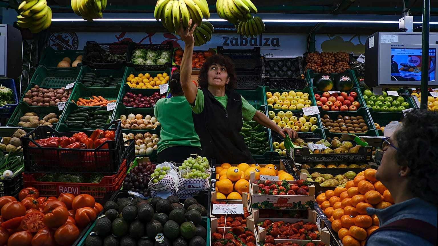 Una trabajadora alcanza un racimo de plátanos mientras un cliente espera, en Pamplona, ​​norte de España, el miércoles 15 de marzo de 2023.