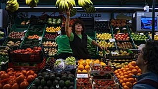 Una trabajadora alcanza un racimo de plátanos mientras un cliente espera, en Pamplona, norte de España, el miércoles 15 de marzo de 2023.
