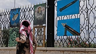 Ένας ένοπλος από την Υεμένη περπατάει μπροστά από πίνακες που απεικονίζουν ρουκέτες και σκηνές αλληλεγγύης στη Γάζα, οι οποίοι εκτίθενται σε έναν φράχτη στην άκρη του δρόμου στη Σαναά, Υεμένη, Δευτέρα 5 Μαΐου 2025. 