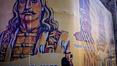 Eine Frau hält ein Mobiltelefon vor dem Hintergrund historischer rumänischer Persönlichkeiten vor der AUR-Zentrale in Bukarest hoch, 4. Mai 2025