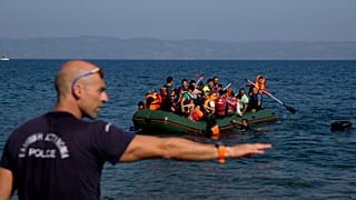 A Greek policeman gives instructions as migrants whose boat stalled at sea while crossing from Turkey to Greece approach the shore of Lesbos, 20 September, 2015