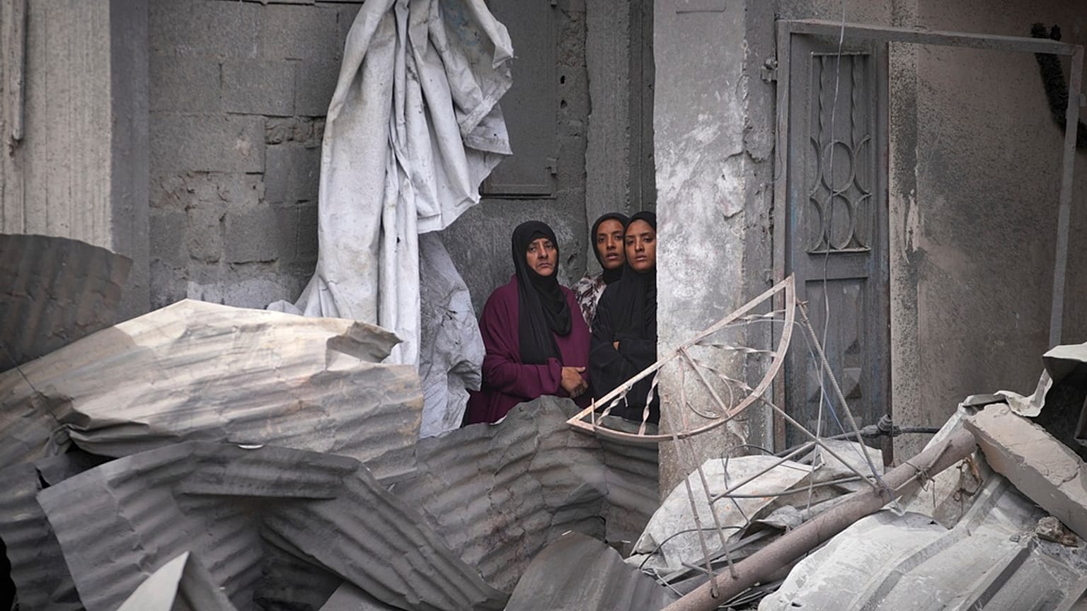 نساء فلسطينيات يراقبن عمليات البحث تحت أنقاض منزل في خان يونس استُهدف بغارة إسرائيلية أسفرت عن مقتل خمسة من عائلة أبو سحلول، 1 مايو 2025.