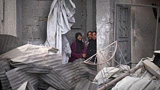 نساء فلسطينيات يراقبن عمليات البحث تحت أنقاض منزل في خان يونس استُهدف بغارة إسرائيلية أسفرت عن مقتل خمسة من عائلة أبو سحلول، 1 مايو 2025.