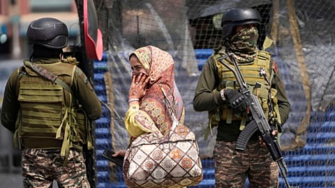 Des soldats indiens montent la garde tandis qu'une femme marche dans un marché à Srinagar, dans la région du Cachemire contrôlée par l'Inde, mercredi 7 mai 2025
