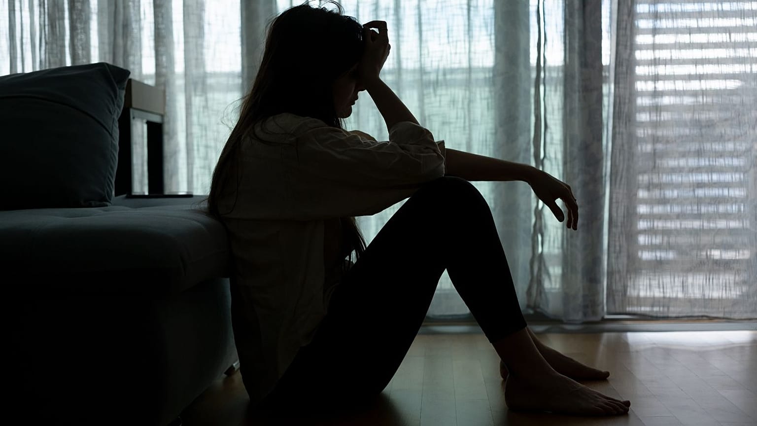 Una mujer angustiada se sienta en la oscuridad.