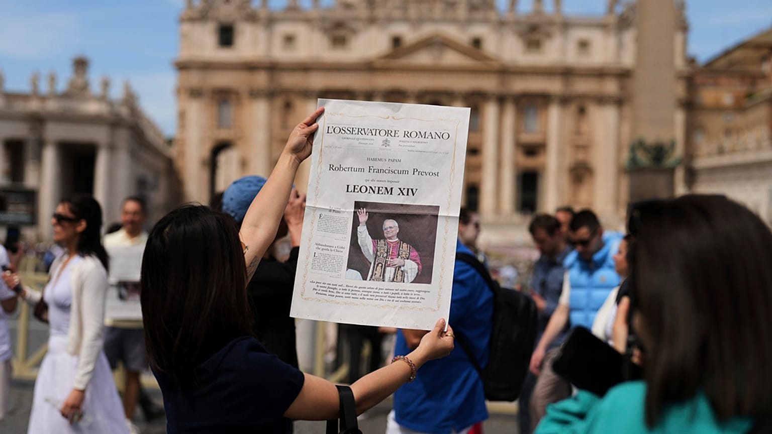 I turisti scattano una foto con l'edizione straordinaria de L'Osservatore Romano con Papa Leone XIV in Vaticano, 9 maggio 2025