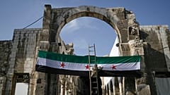 عامل يرفع علم "الثورة" السورية عند مدخل الجامع الأموي قبيل صلاة الجمعة في دمشق، 20 ديسمبر 2024.
