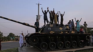 Pakistanis flash victory signs as they celebrate on top of a model of a tank following India and Pakistan have reached a ceasefire deal, in Multan, 10 May 2025