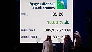 شركة النفط السعودية المملوكة للدولة أرمكو ومسؤولو سوق الأسهم يسيرون تحت شاشة تعرض القيمة المتداولة وحجم التداول في الطرح العام الأولي لأرامكو في سوق الأسهم بالرياض 