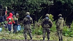 Migranten, die an der polnisch-weißrussischen Grenze gestrandet sind, tragen Plastikwasserflaschen und sind von polnischen Einsatzkräften in Usnarz Górny, Polen, umgeben, Mittwoch, 1. September 2021