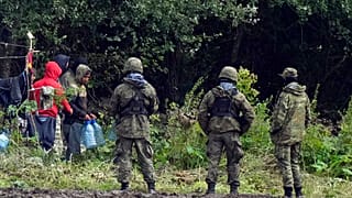 Migranci utknęli na granicy polsko-białoruskiej, niosąc plastikowe butelki z wodą, otoczeni przez polskie siły w Usnarzu Górnym w Polsce, w środę, 1 września 2021 roku