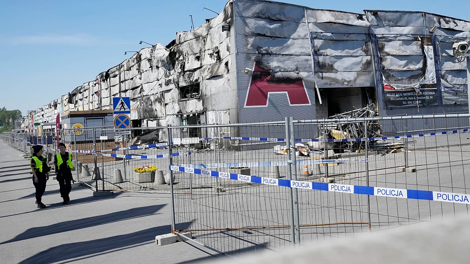 Polizisten gehen an einem provisorischen Zaun vorbei, der errichtet wurde, um den Zugang zu einem niedergebrannten Einkaufszentrum in Warschau, Polen, zu versperren, 15. Mai 2024.