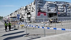 Polizisten gehen an einem provisorischen Zaun vorbei, der errichtet wurde, um den Zugang zu einem niedergebrannten Einkaufszentrum in Warschau, Polen, zu versperren, 15. Mai 2024.