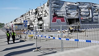 La policía camina junto a una valla temporal colocada para bloquear el acceso a un centro comercial incendiado en Varsovia, Polonia, 15 de mayo de 2024.
