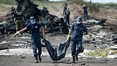  Rus yanlısı savaşçılar Malezya Havayolları'na ait MH17 sefer sayılı uçağın düştüğü yerde nöbet tutarken Ukraynalı Acil Yardım çalışanları bir kurbanın cesedini ceset torbasında taşıyor, 20 Temmuz 2014.