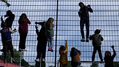 Kinder klettern an einem Zaun um einen Fußballplatz. Je nach Wohnort und Wohlstand steht ihnen eine unterschiedliche Zukunft bevor.