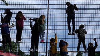 Kinder klettern an einem Zaun um einen Fußballplatz. Je nach Wohnort und Wohlstand steht ihnen eine unterschiedliche Zukunft bevor.