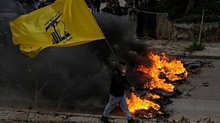 مؤيد لحزب الله يحمل علم الحزب بينما يحرق آخرون الإطارات لإغلاق طريق المطار الدولي خلال احتجاج يوم الجمعة 7 فبراير 2025.AP Photo/Bilal Hussein